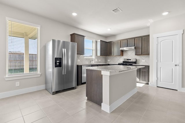 kitchen featuring light tile patterned floors, appliances with stainless steel finishes, a center island, light stone counters, and dark brown cabinetry