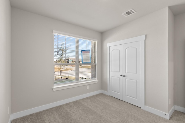 unfurnished bedroom featuring multiple windows, light colored carpet, and a closet