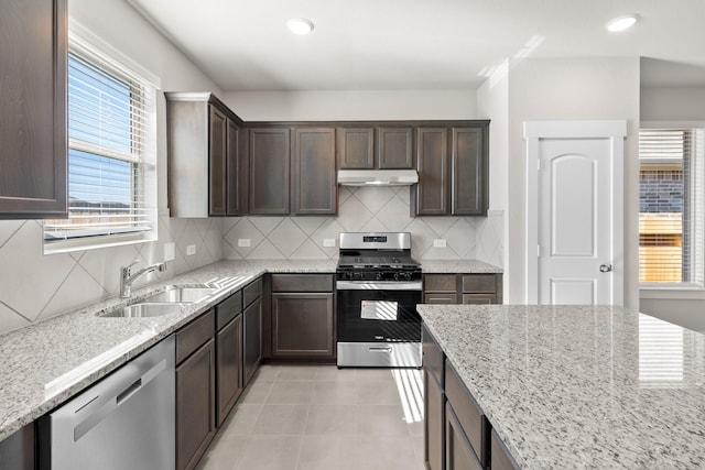 kitchen with appliances with stainless steel finishes, dark brown cabinetry, under cabinet range hood, and a sink