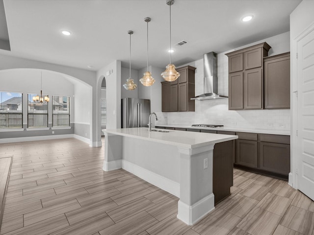 kitchen featuring pendant lighting, appliances with stainless steel finishes, wall chimney exhaust hood, and an island with sink