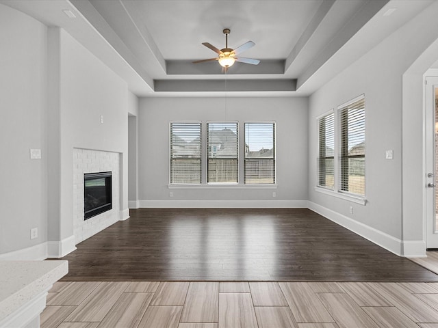 unfurnished living room featuring ceiling fan, a tray ceiling, and a brick fireplace