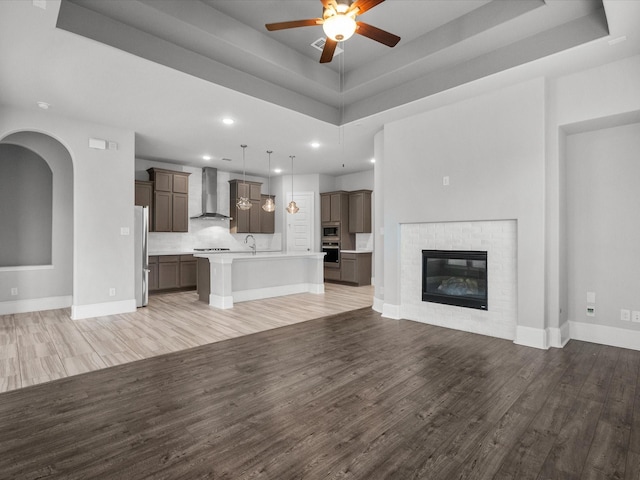 unfurnished living room featuring a tiled fireplace, hardwood / wood-style floors, and a tray ceiling