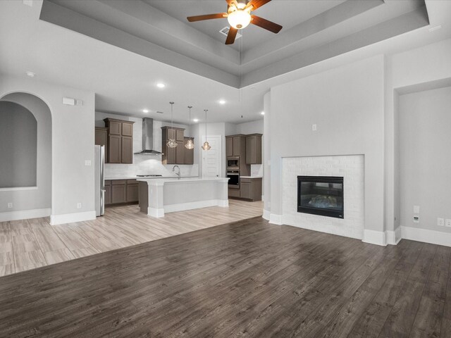 unfurnished living room featuring a fireplace, wood-type flooring, and a tray ceiling