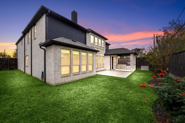 back house at dusk with a patio and a lawn