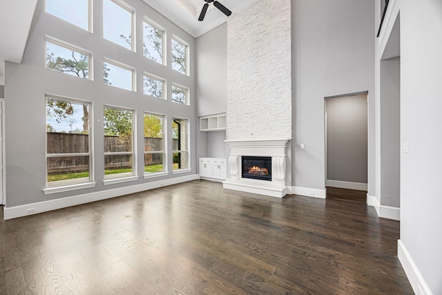 unfurnished living room with a towering ceiling, a fireplace, dark wood-type flooring, and plenty of natural light