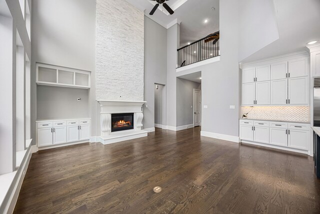 unfurnished living room with a high ceiling, ceiling fan, dark wood-type flooring, and a fireplace