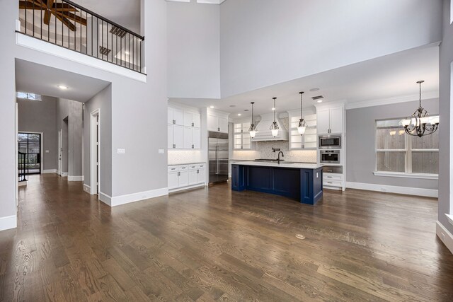 unfurnished living room featuring a towering ceiling, sink, an inviting chandelier, and dark wood-type flooring