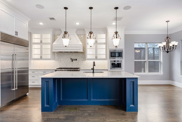 kitchen with sink, white cabinetry, a kitchen island with sink, built in appliances, and custom range hood