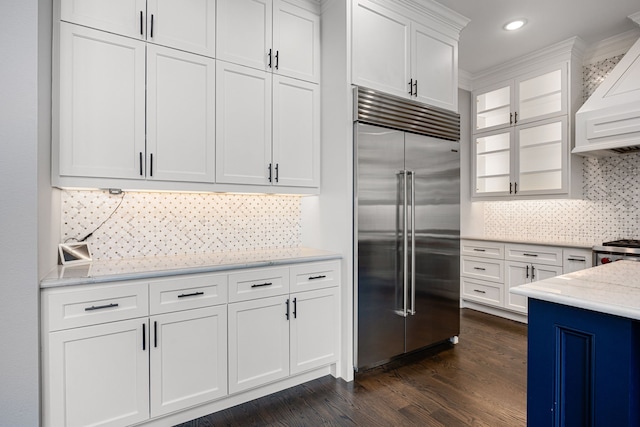 kitchen featuring dark wood-type flooring, light stone counters, built in refrigerator, decorative backsplash, and white cabinets