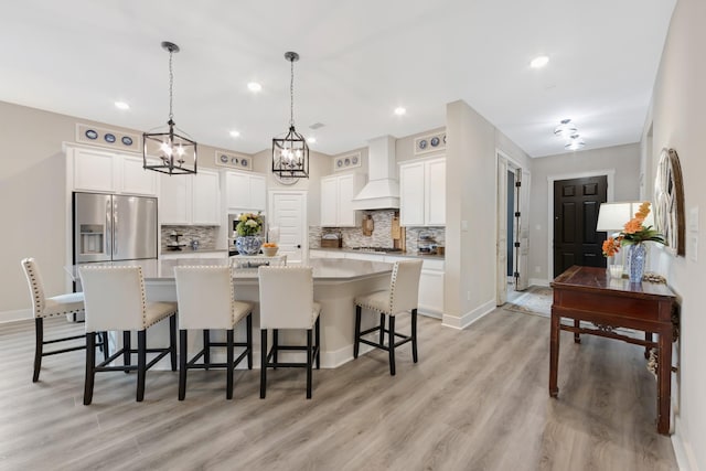 kitchen with a center island with sink, appliances with stainless steel finishes, custom range hood, pendant lighting, and decorative backsplash