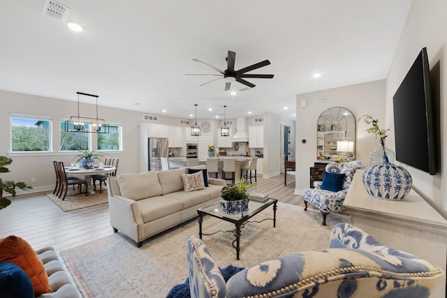 living room featuring ceiling fan with notable chandelier and light hardwood / wood-style flooring