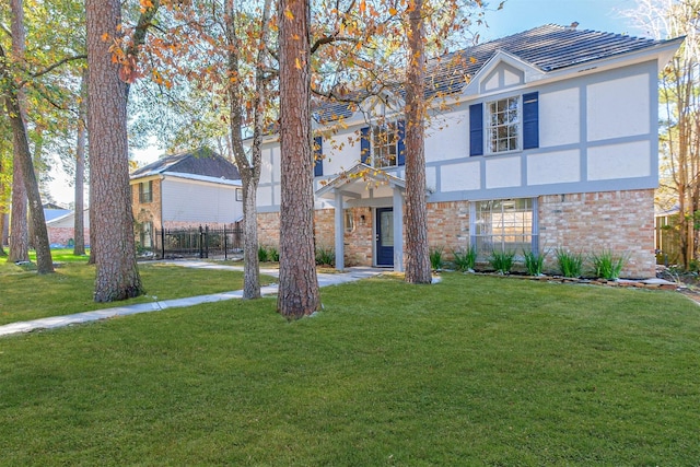 tudor home with brick siding, a front yard, fence, and stucco siding