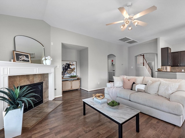 living room featuring dark wood-type flooring, ceiling fan, and a tiled fireplace