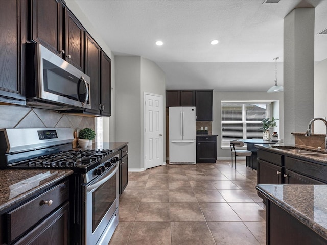 kitchen featuring sink, stainless steel appliances, hanging light fixtures, and dark stone counters