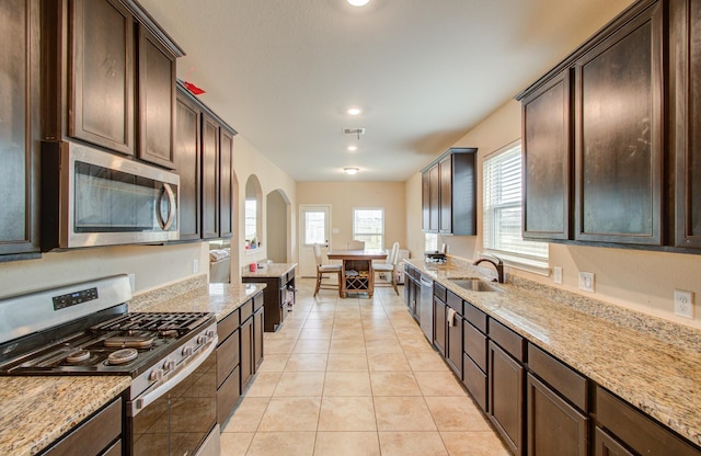 kitchen featuring light tile patterned flooring, sink, stainless steel appliances, light stone countertops, and dark brown cabinets