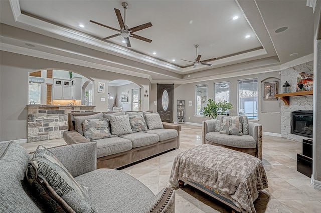 living room with ceiling fan, a fireplace, ornamental molding, and a tray ceiling