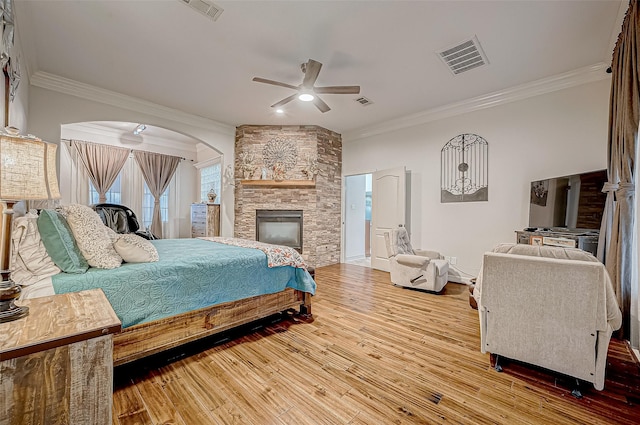 bedroom with crown molding, a stone fireplace, ceiling fan, and hardwood / wood-style flooring