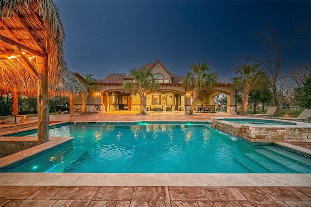 pool at twilight with an in ground hot tub, pool water feature, and a patio