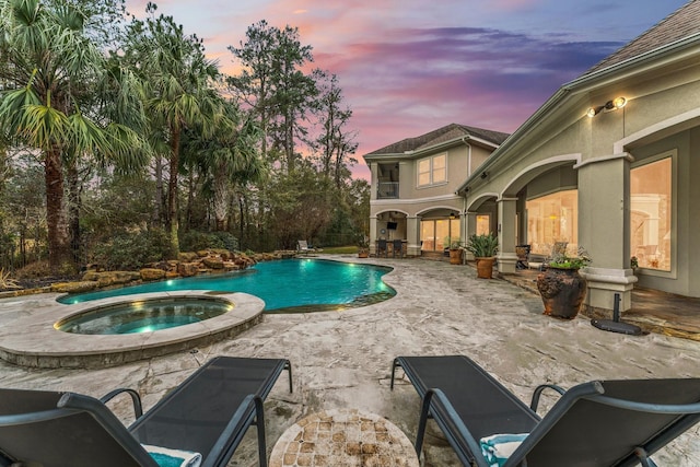 pool at dusk with an in ground hot tub and a patio