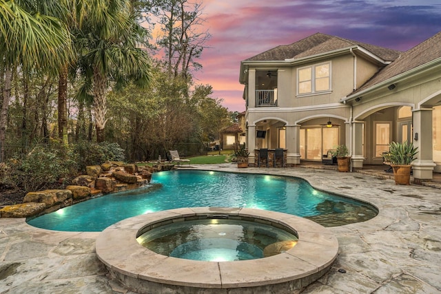 pool at dusk with a patio area, an outdoor bar, ceiling fan, and an in ground hot tub