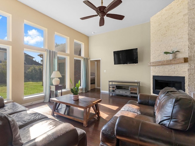 living room featuring ceiling fan, dark hardwood / wood-style floors, and a stone fireplace