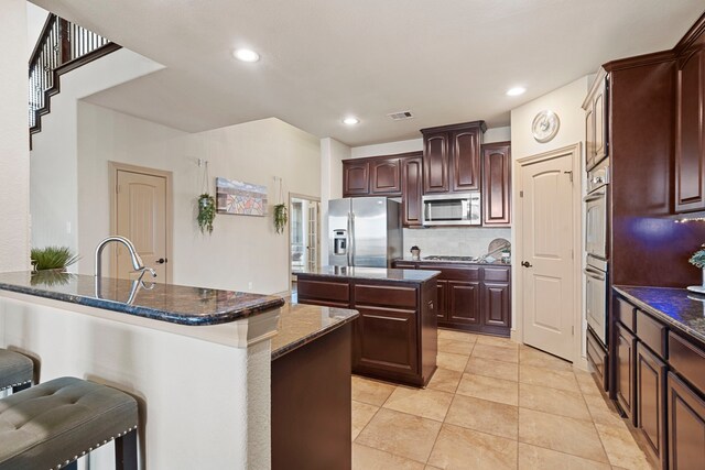 kitchen featuring appliances with stainless steel finishes, sink, dark stone countertops, backsplash, and a center island