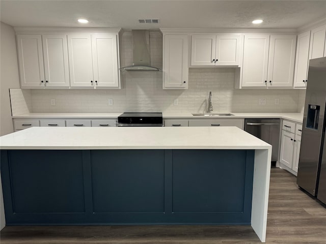 kitchen with sink, stainless steel appliances, white cabinets, a kitchen island, and wall chimney exhaust hood