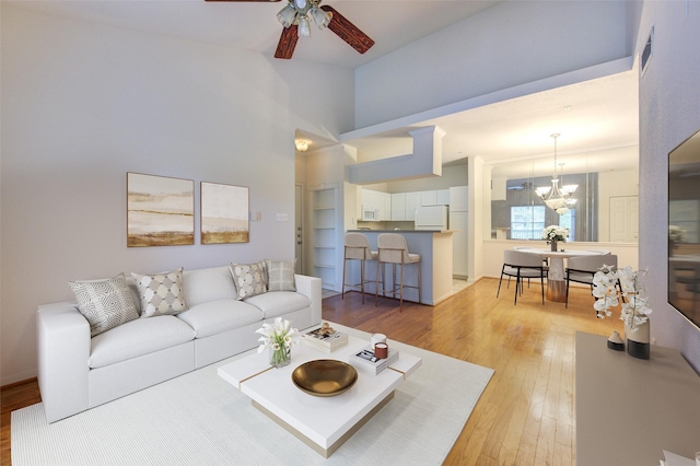 living room with ceiling fan with notable chandelier and light hardwood / wood-style flooring