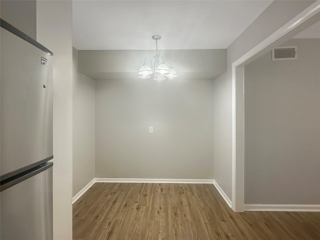 unfurnished dining area featuring a notable chandelier and wood-type flooring