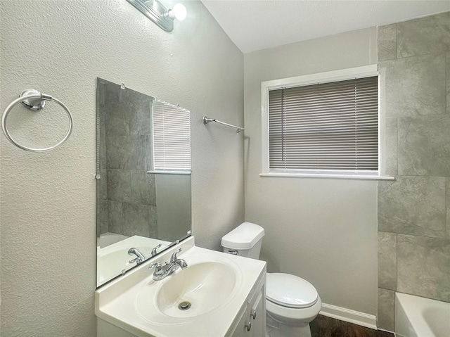 full bathroom featuring toilet, a bathing tub, baseboards, and vanity