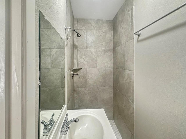 full bath featuring a tile shower and a sink