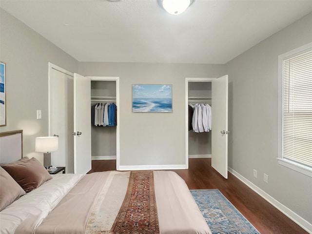 bedroom with multiple windows, baseboards, two closets, and wood finished floors