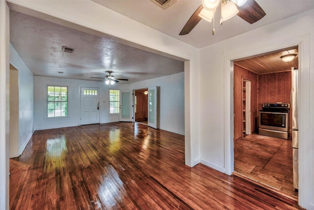 unfurnished living room featuring ceiling fan, dark hardwood / wood-style flooring, and wood walls