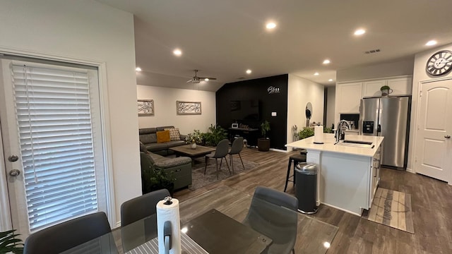 kitchen featuring stainless steel fridge, a kitchen island with sink, white cabinetry, a kitchen breakfast bar, and dark hardwood / wood-style floors