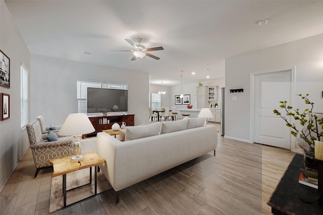 living room featuring a healthy amount of sunlight, ceiling fan with notable chandelier, and light wood-type flooring