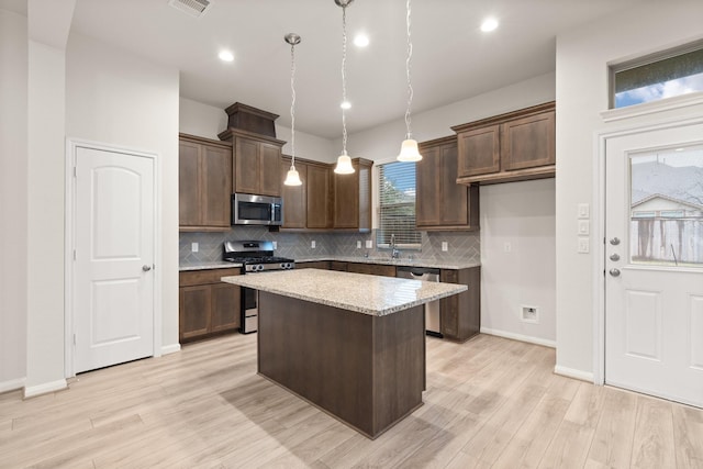 kitchen featuring hanging light fixtures, a center island, stainless steel appliances, light stone countertops, and light wood-type flooring