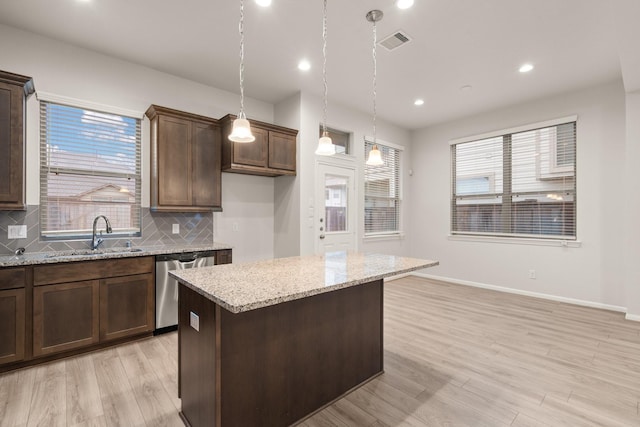 kitchen with a kitchen island, decorative light fixtures, sink, stainless steel dishwasher, and light stone counters