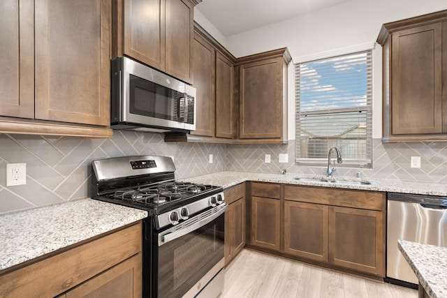 kitchen with sink, light hardwood / wood-style flooring, appliances with stainless steel finishes, light stone counters, and tasteful backsplash