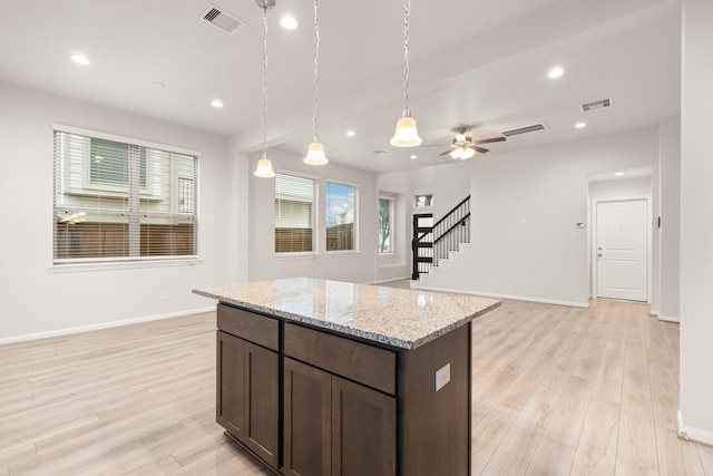 kitchen with pendant lighting, dark brown cabinets, light stone countertops, and light hardwood / wood-style flooring