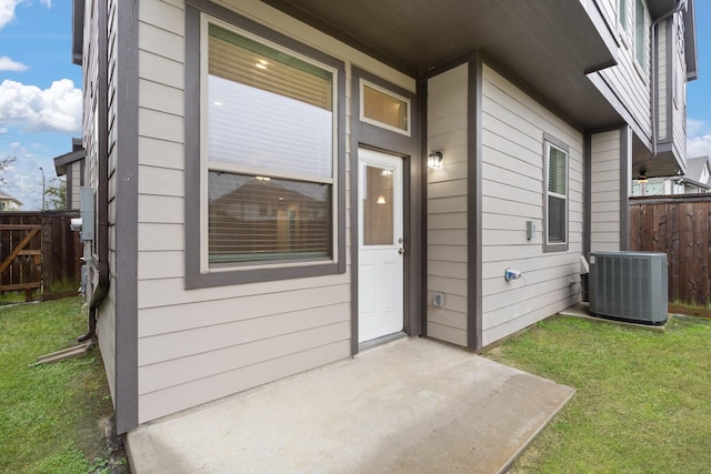 view of exterior entry with a yard, a patio area, and central air condition unit