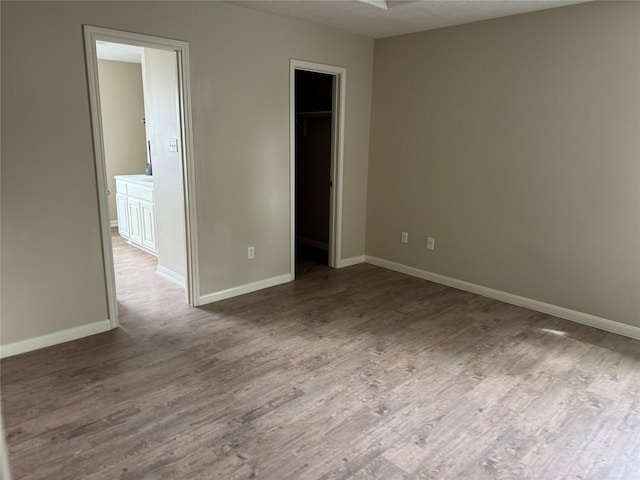 unfurnished bedroom featuring ensuite bath, a spacious closet, a textured ceiling, a closet, and hardwood / wood-style flooring