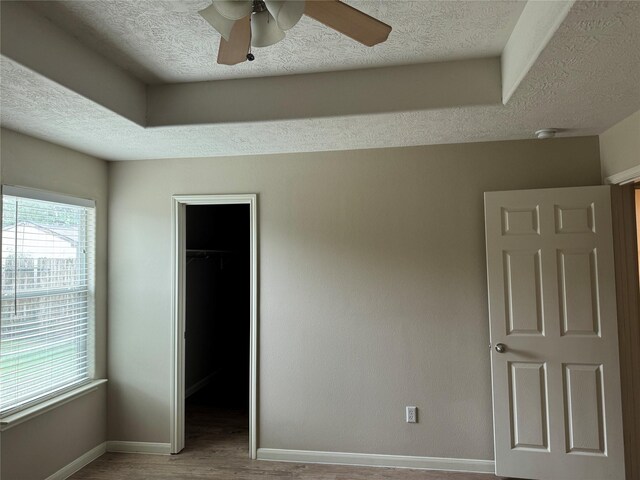 unfurnished bedroom with ceiling fan, a walk in closet, multiple windows, and a closet