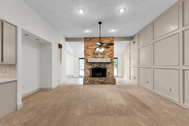 unfurnished living room with lofted ceiling with beams, light carpet, a textured ceiling, ceiling fan, and a fireplace