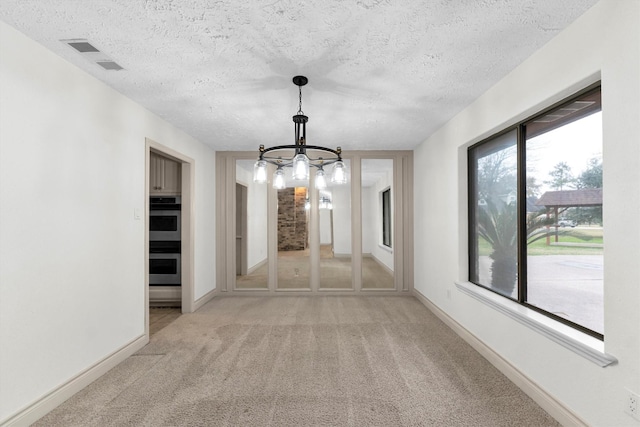 hallway with a notable chandelier, plenty of natural light, light colored carpet, and a textured ceiling