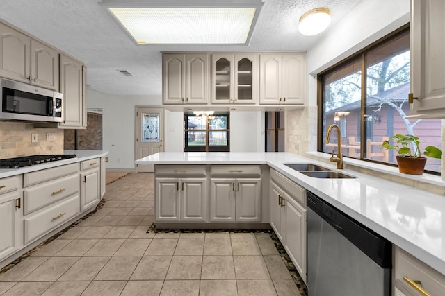 kitchen featuring sink, light tile patterned floors, appliances with stainless steel finishes, kitchen peninsula, and decorative backsplash