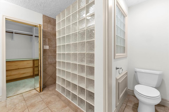 bathroom with walk in shower, toilet, tile patterned flooring, and a textured ceiling