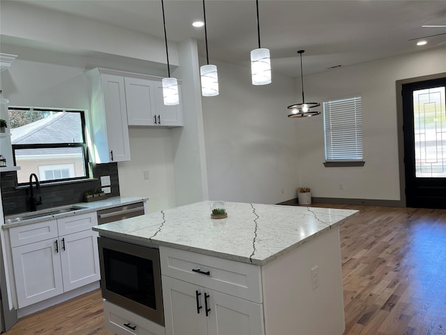 kitchen featuring built in microwave, white cabinetry, decorative backsplash, hanging light fixtures, and a center island