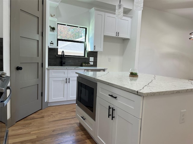 kitchen with white cabinetry, sink, light stone counters, and hanging light fixtures