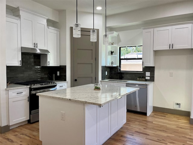 kitchen featuring white cabinetry, hanging light fixtures, stainless steel appliances, light stone countertops, and a kitchen island