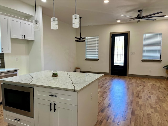 kitchen with built in microwave, light stone counters, decorative light fixtures, and white cabinets